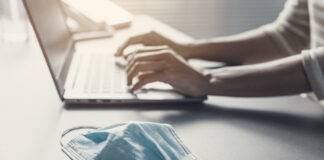 Office worker typing on a laptop and face mask