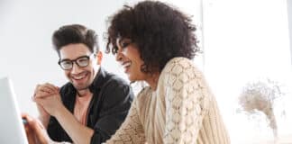 Cheerful young colleagues using laptop computer together