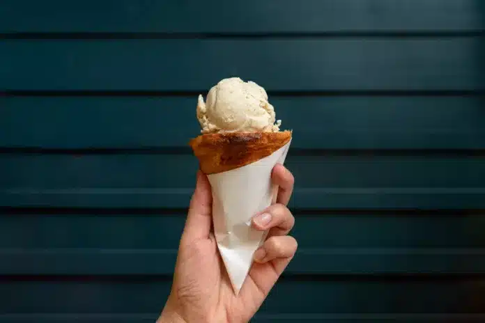 Scoop of sweet ice cream on croissant cone with wooden dark green wall background.